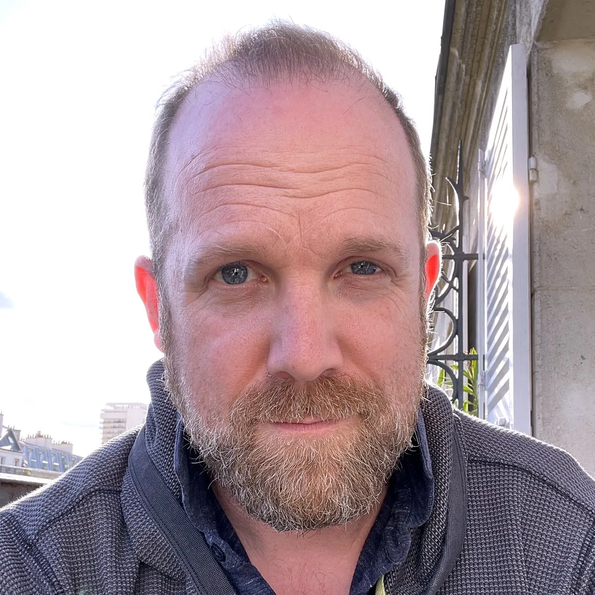 Andrew Jaspersohn outdoors on a sunny balcony, wearing a grey knit jacket.